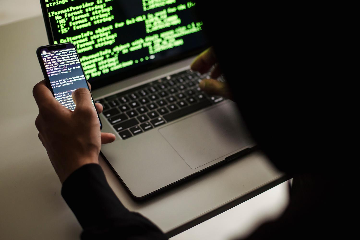 Persona utilizando simultáneamente un smartphone y un portátil con terminal, representando el flujo de trabajo de introducir un código 2FA.