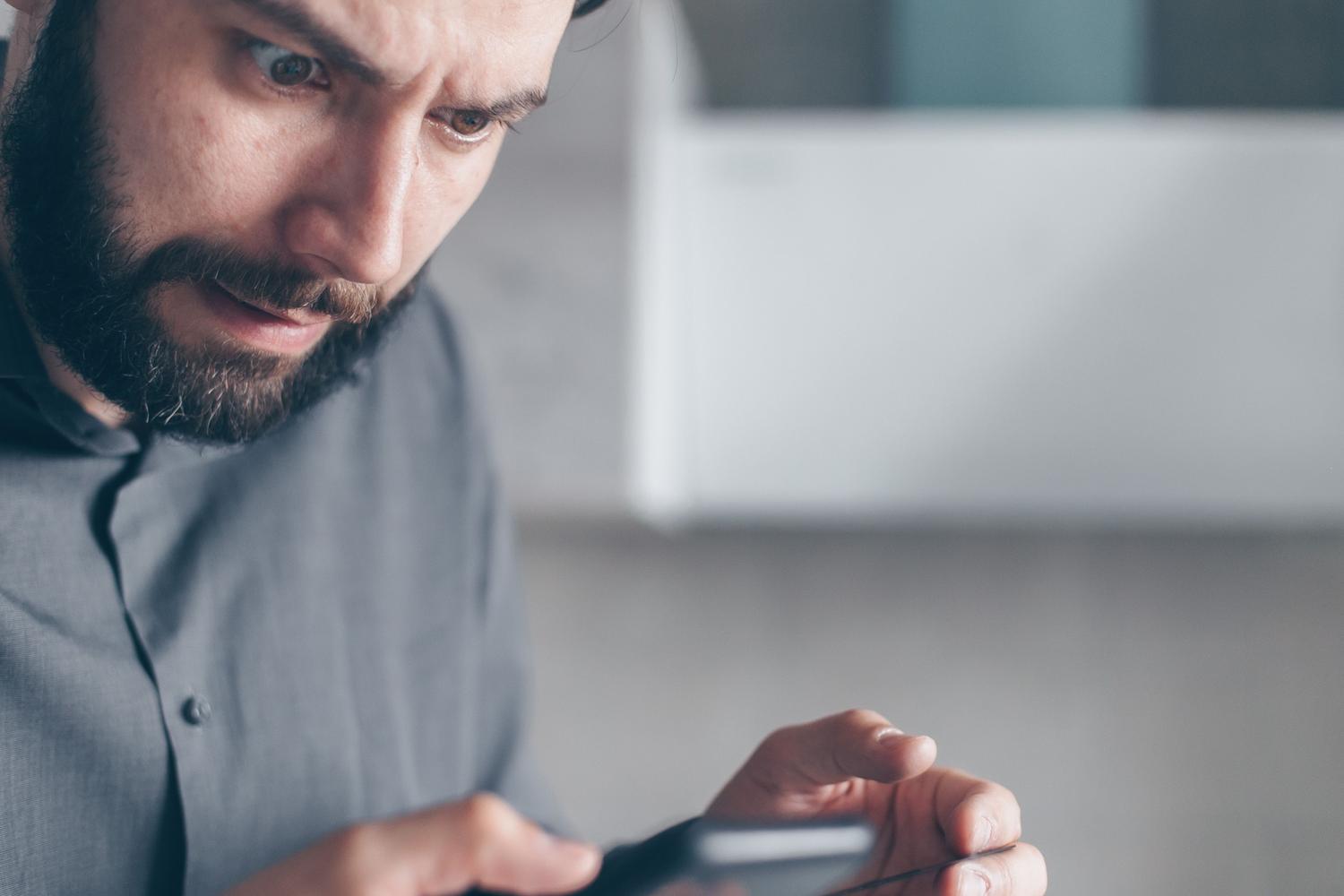 Hombre sorprendido al recibir una alerta de emergencia en su teléfono móvil, representando el pánico inicial y el riesgo de descartar notificaciones por error.