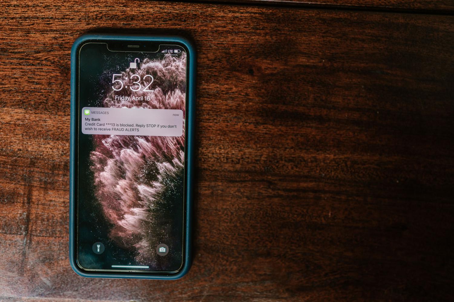 Primer plano de un smartphone con una notificación de alerta en la pantalla sobre una superficie de madera.