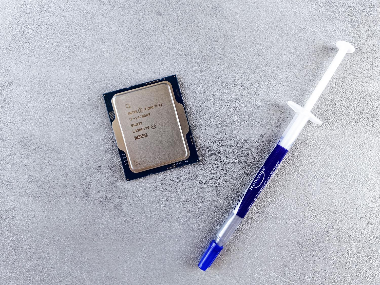 Detalle de un procesador Intel Core i7 junto a una jeringa de pasta térmica sobre una superficie neutra. Detalle de un procesador Intel Core i7 junto a una jeringa de pasta térmica sobre una superficie neutra.