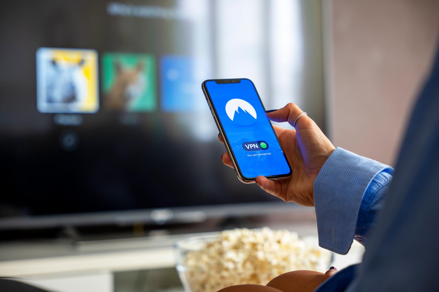 Person checking internet connection on a smartphone with a streaming TV in the background.