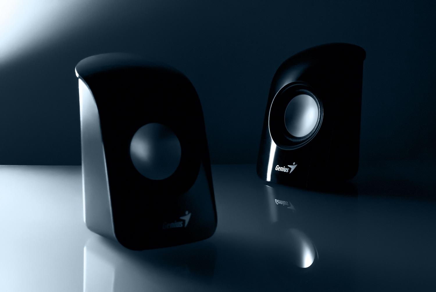 Detalle de altavoces multimedia modernos sobre una superficie reflectante, ilustrando el hardware de salida de audio.