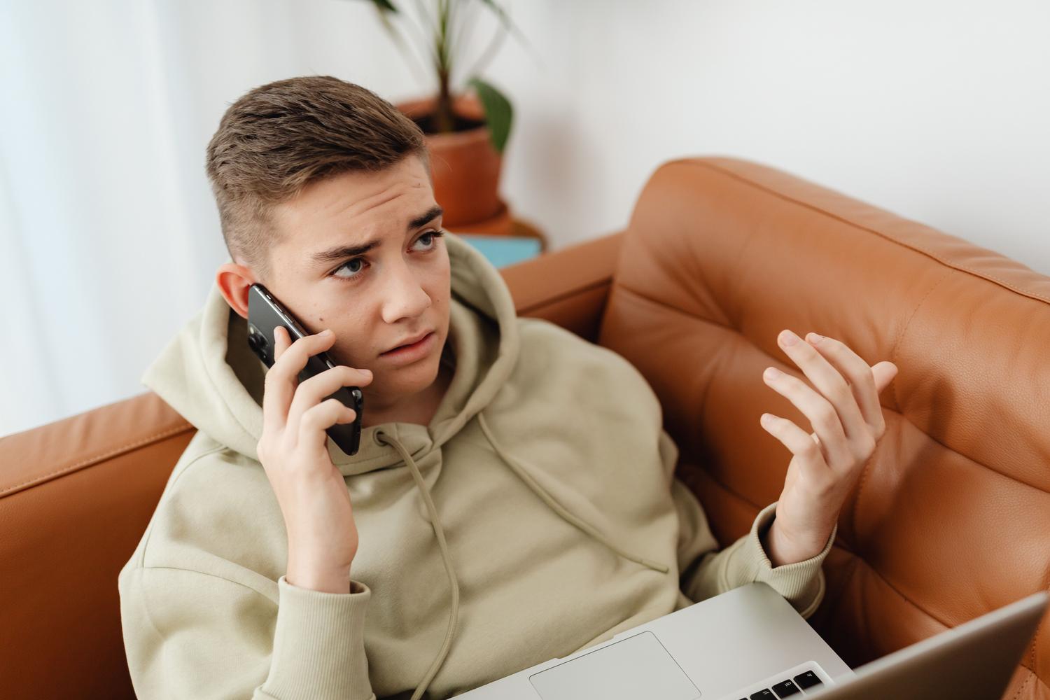 Joven frustrado usando un portátil y un teléfono móvil simultáneamente, representando la tensión de enfrentarse a un problema técnico como el almacenamiento de iCloud lleno.