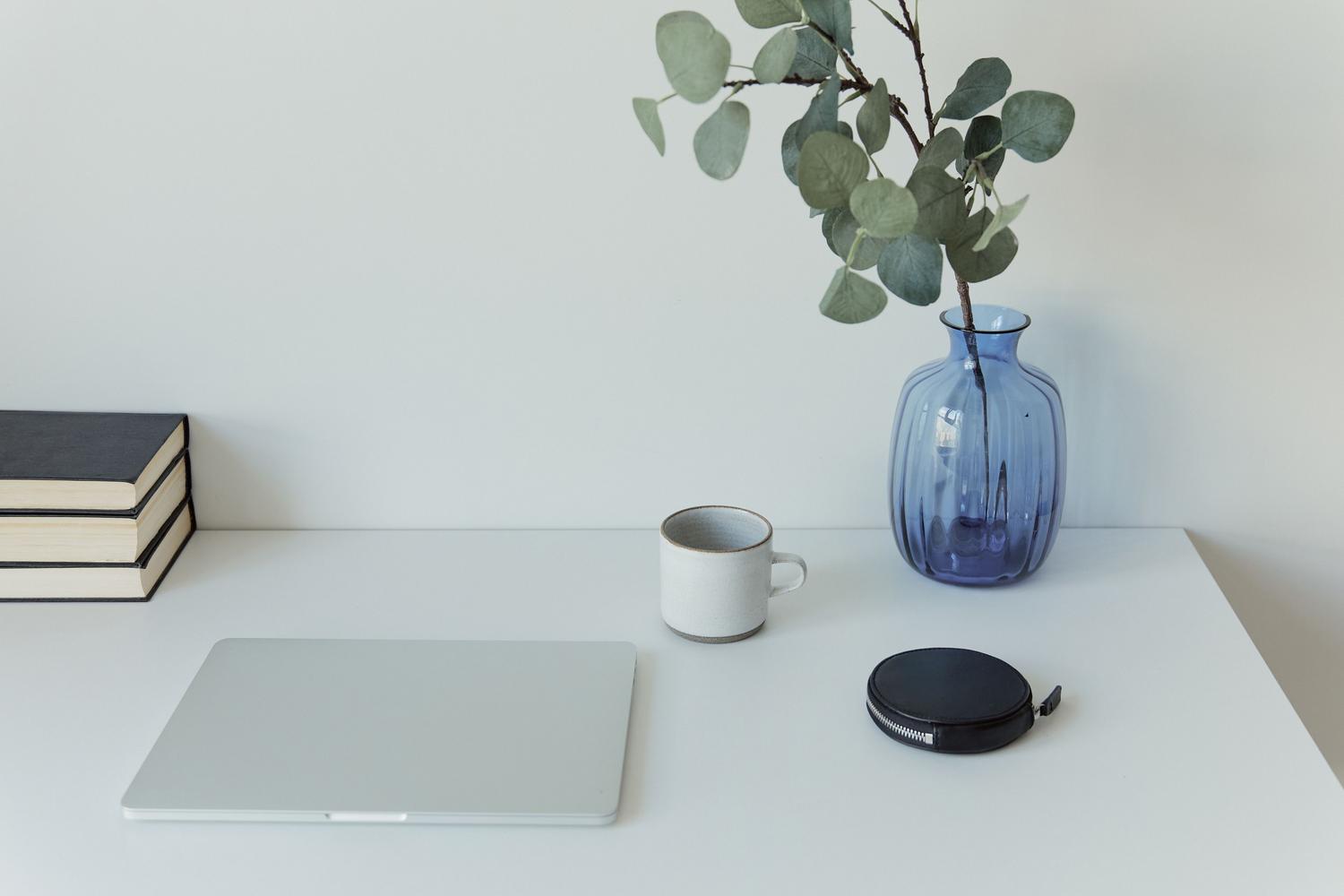 Espacio de trabajo extremadamente minimalista en blanco con un portátil cerrado y libros, representando la claridad mental y el orden