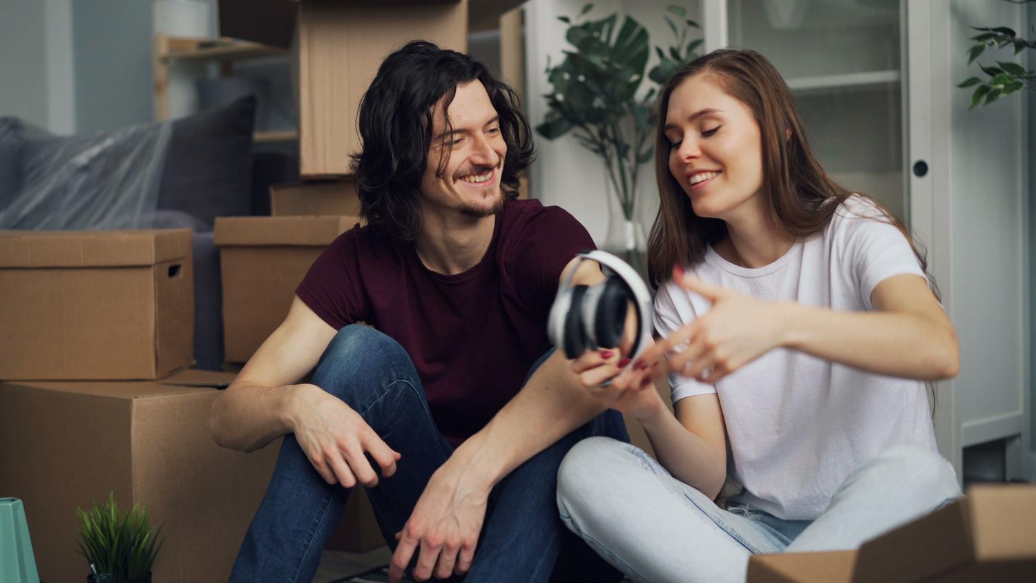 Pareja feliz disfrutando de audio compartido con auriculares Bluetooth en un ambiente hogareño