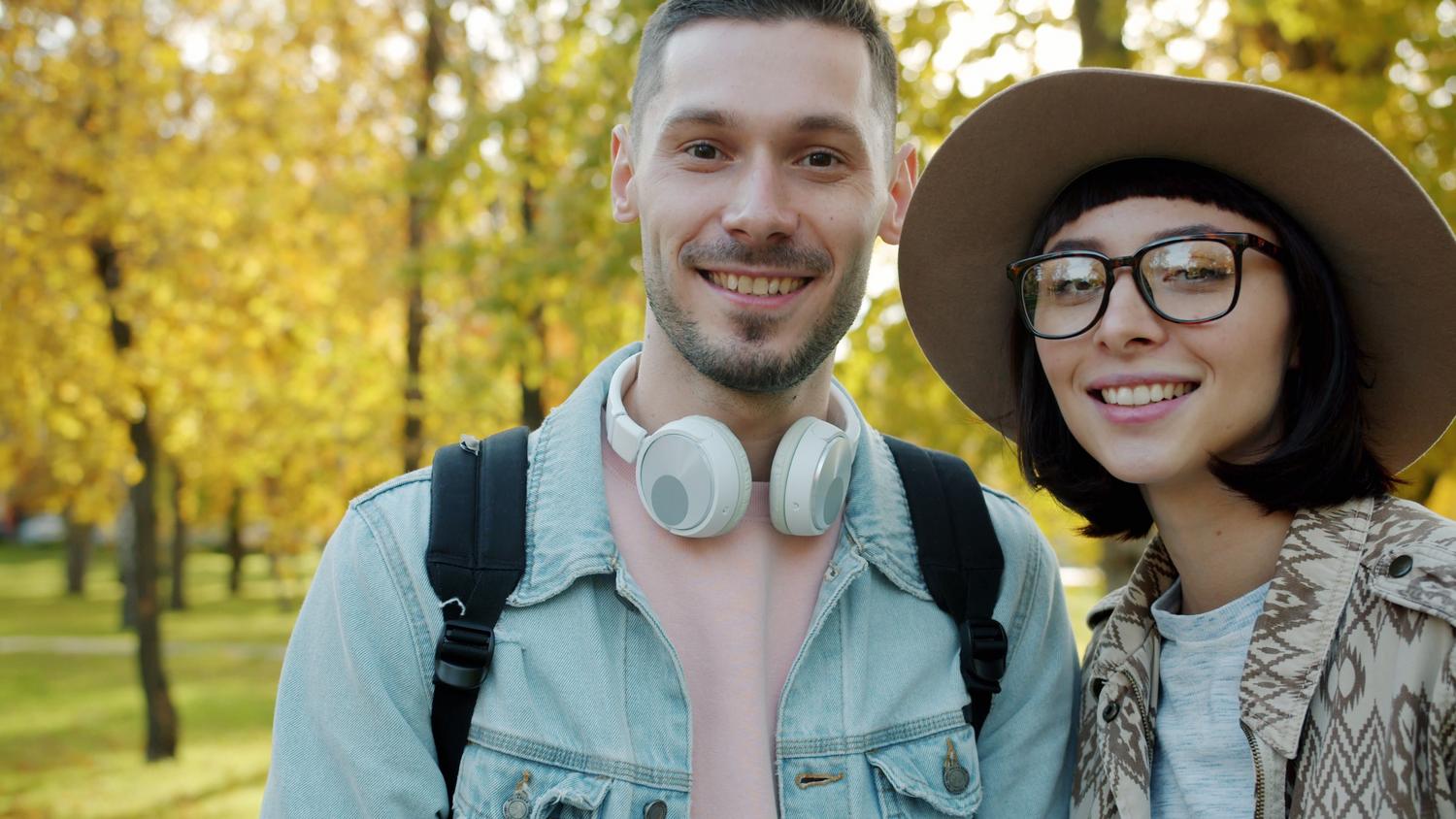 Pareja joven paseando por un parque en otoño con auriculares inalámbricos