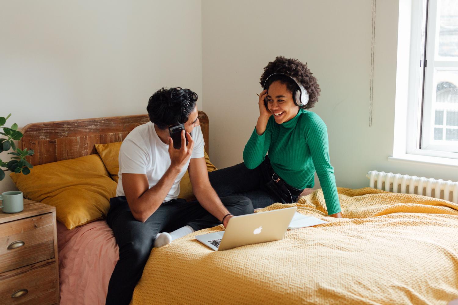 Pareja usando un ordenador portátil y auriculares inalámbricos en una habitación luminosa
