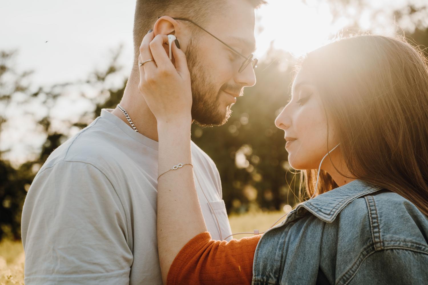Pareja joven compartiendo música al aire libre con auriculares inalámbricos durante el atardecer