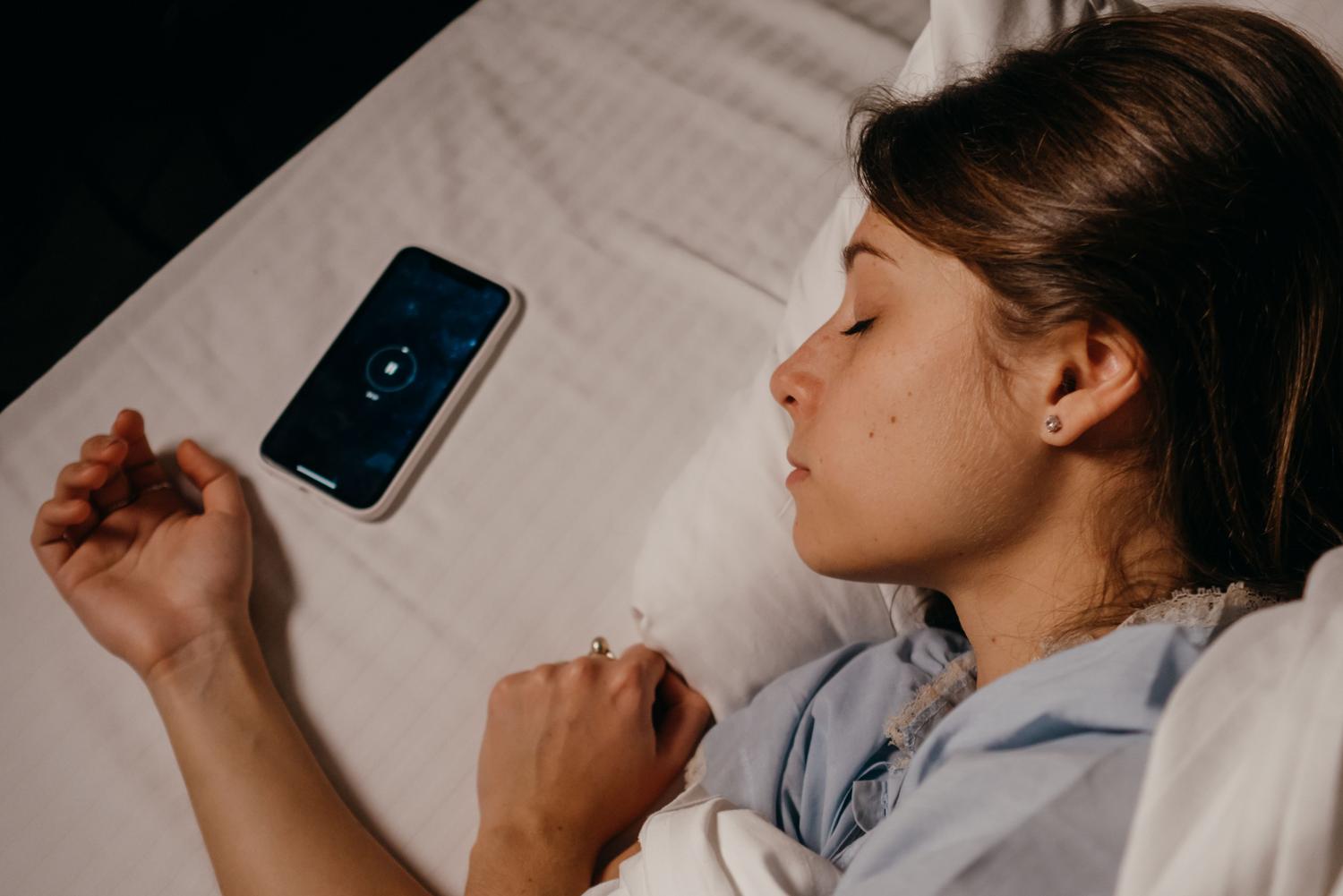 Mujer durmiendo plácidamente en la cama con su teléfono móvil al lado, representando el equilibrio digital.