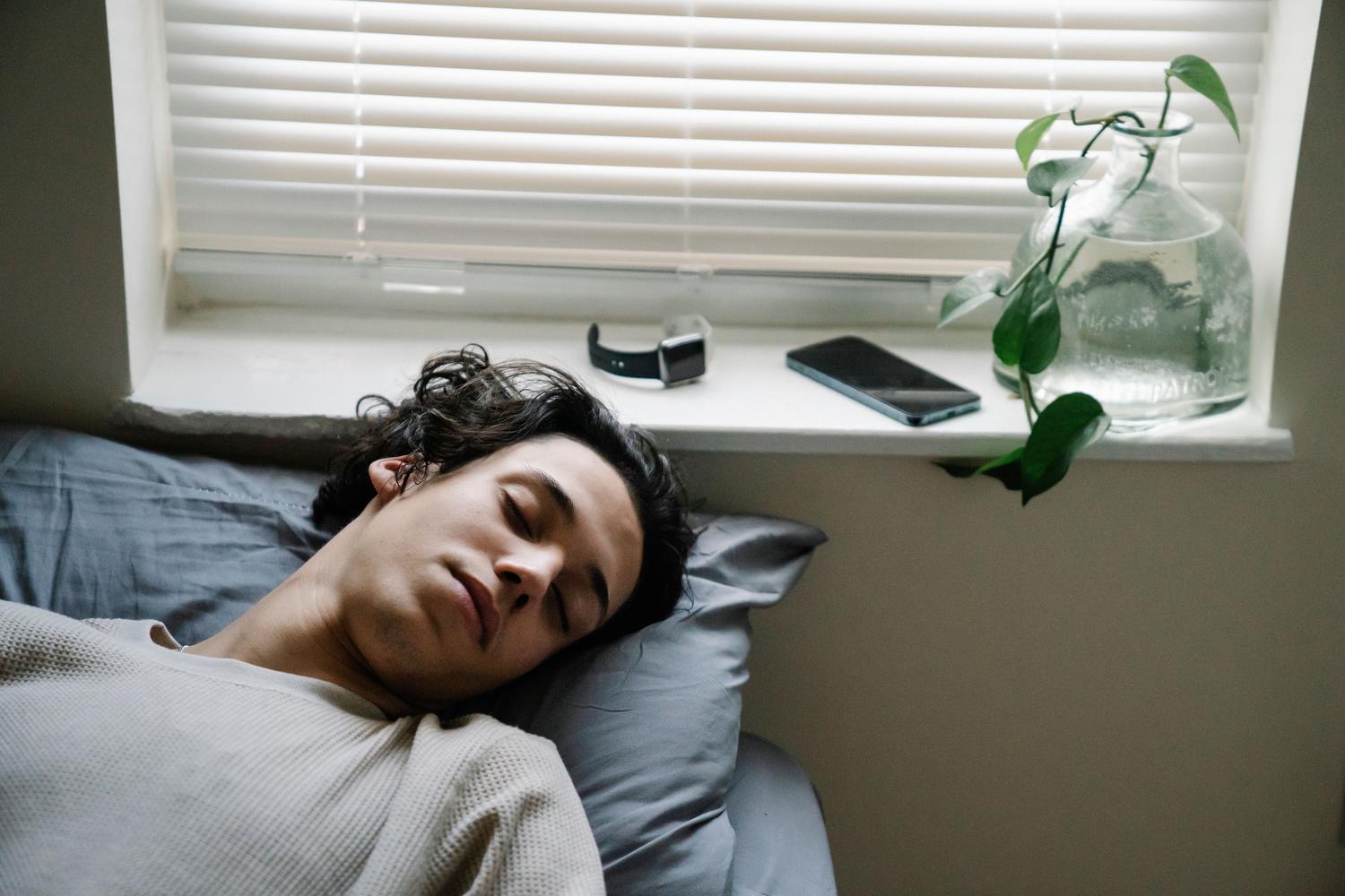 Hombre descansando con un smartphone y un reloj inteligente cerca, ilustrando la sincronización de dispositivos.