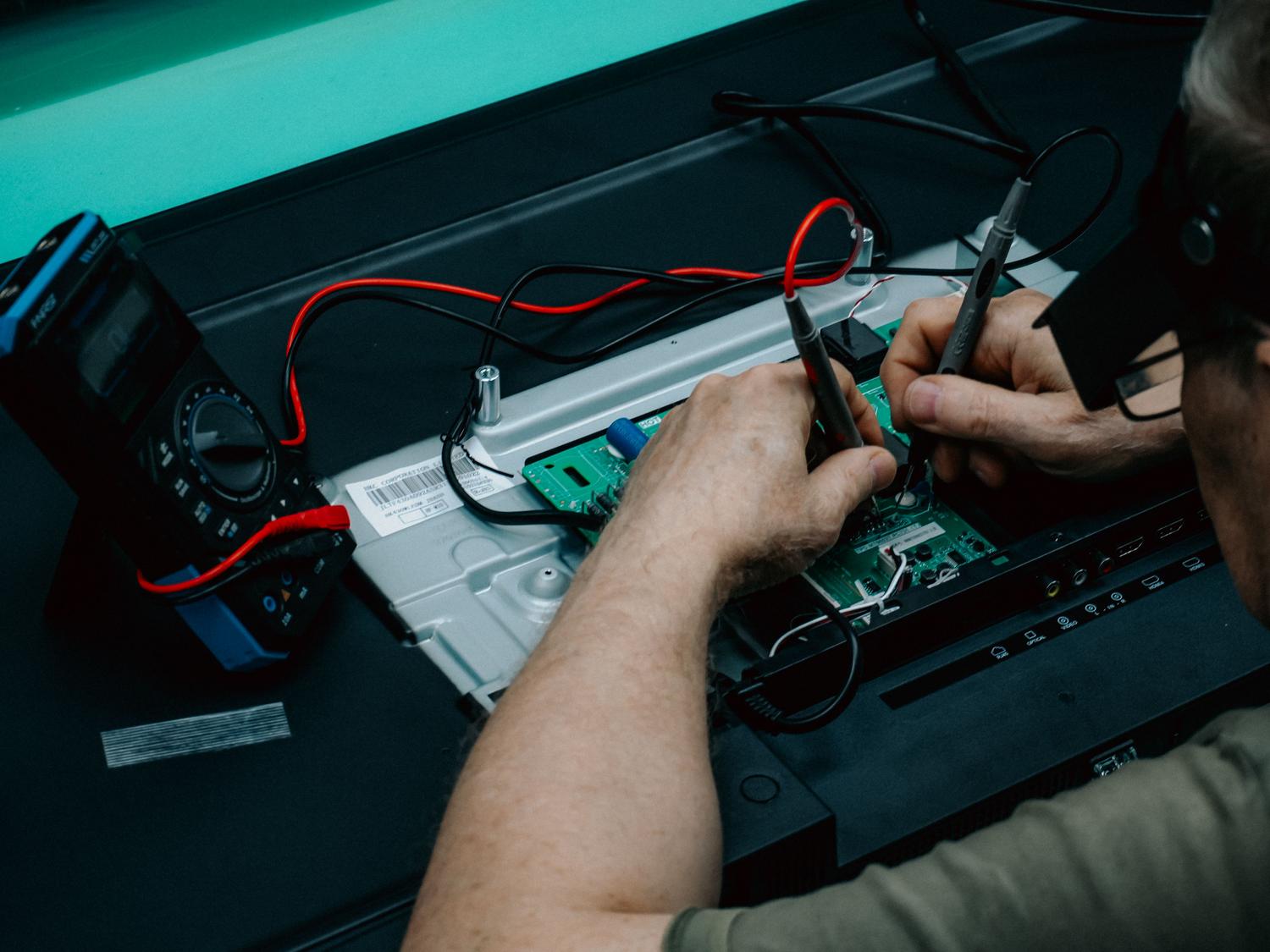 Técnico utilizando un multímetro para diagnosticar fallos en la placa electrónica de un televisor.