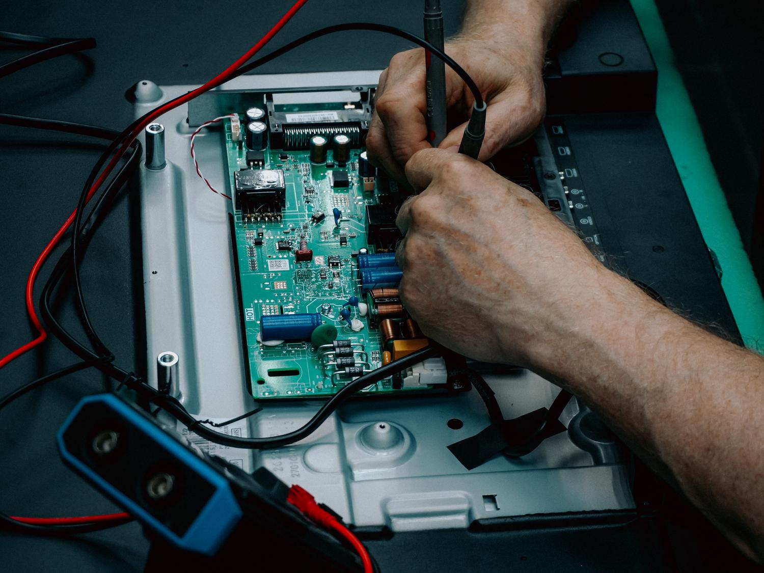 Técnico reparando una placa de circuito electrónico con herramientas de precisión.