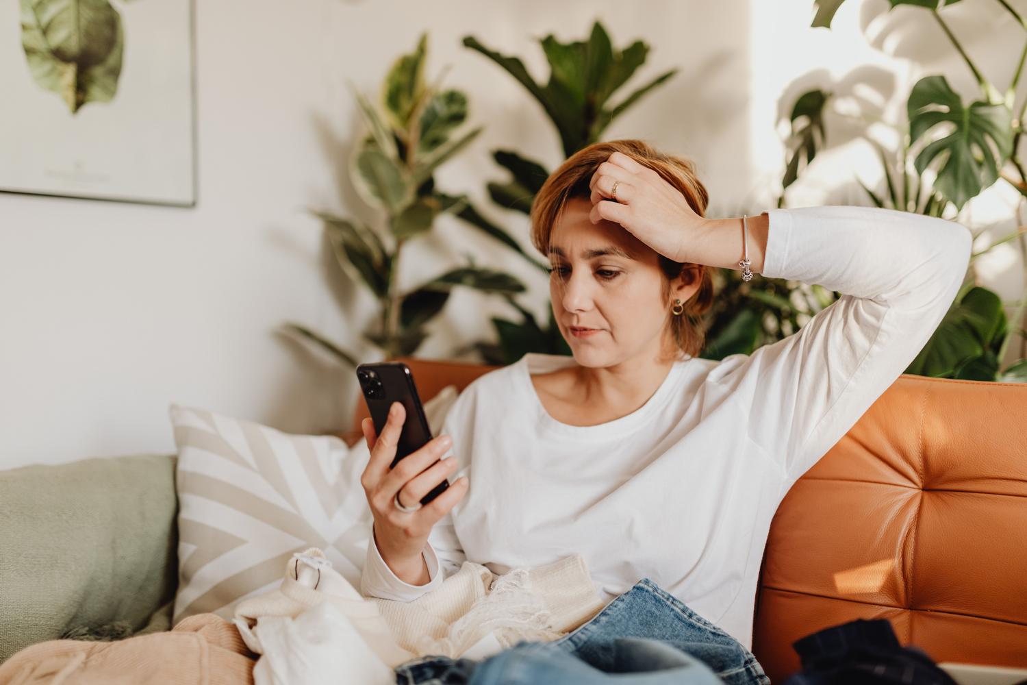 Mujer confundida revisando su smartphone, ilustrando la búsqueda de soluciones a fallos del sistema.