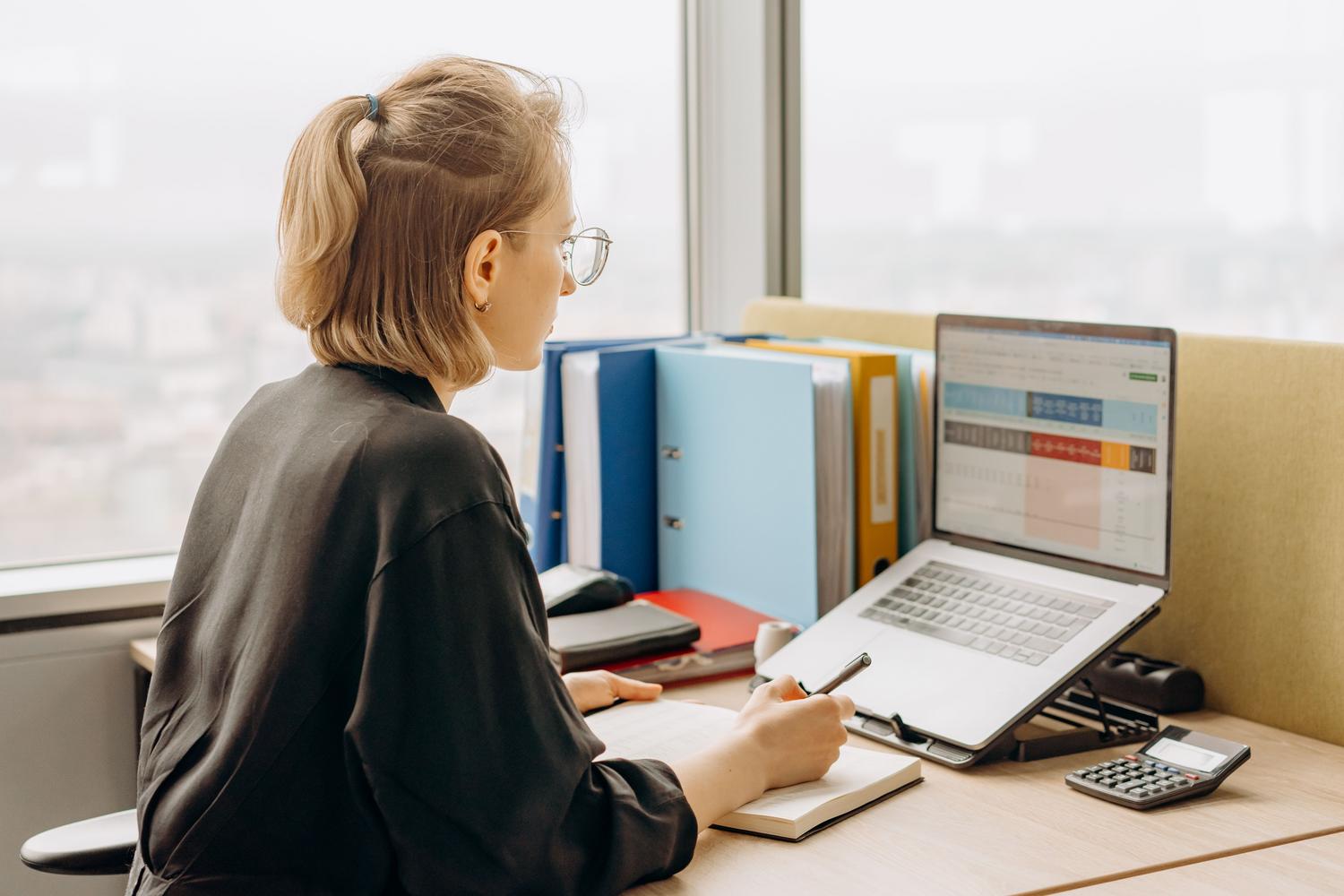 Mujer profesional trabajando con hojas de cálculo complejas en un entorno de oficina moderno.