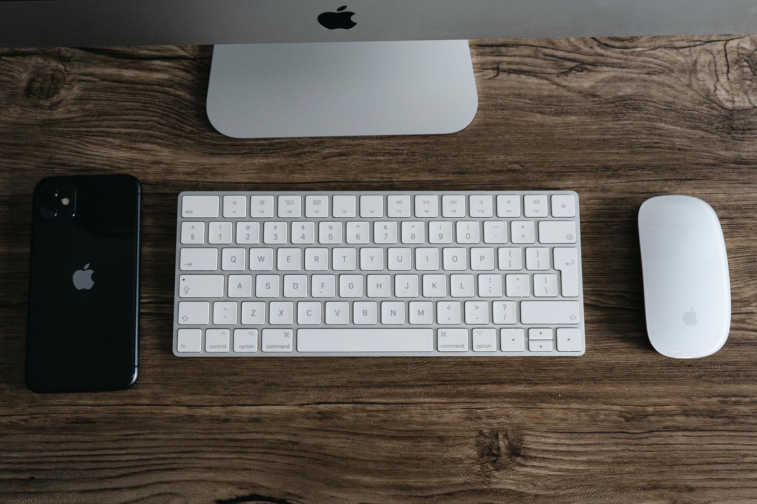 Espacio de trabajo minimalista con dispositivos Apple sobre una mesa de madera, representando la organización y productividad.