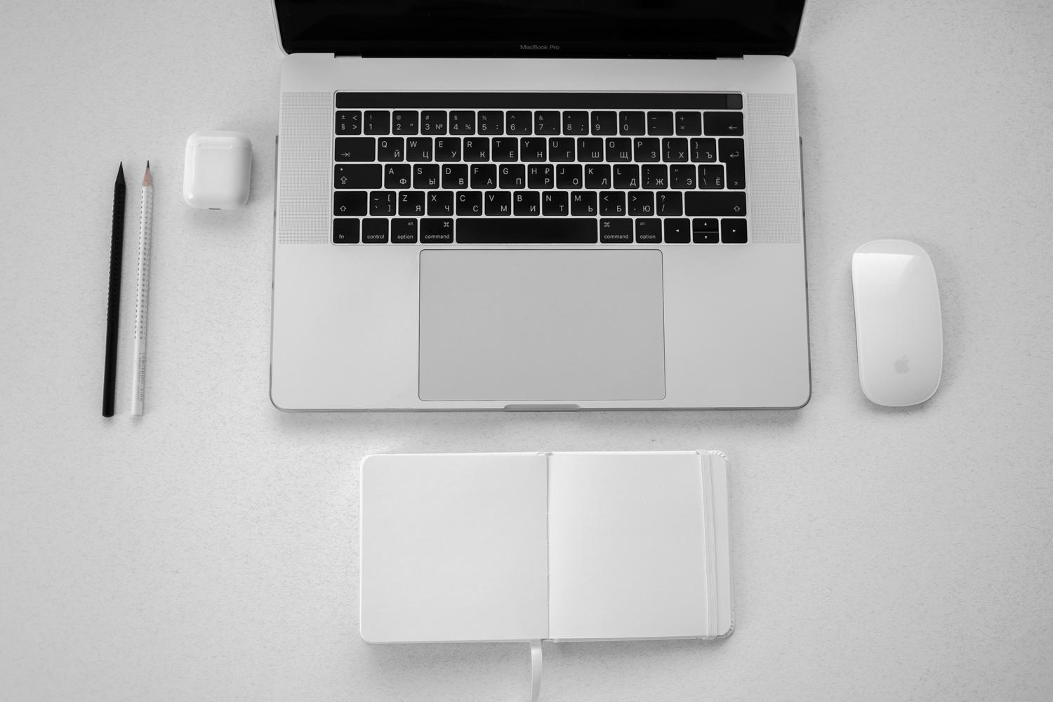 Vista cenital de un espacio de trabajo productivo con MacBook, cuaderno y mouse inalámbrico.