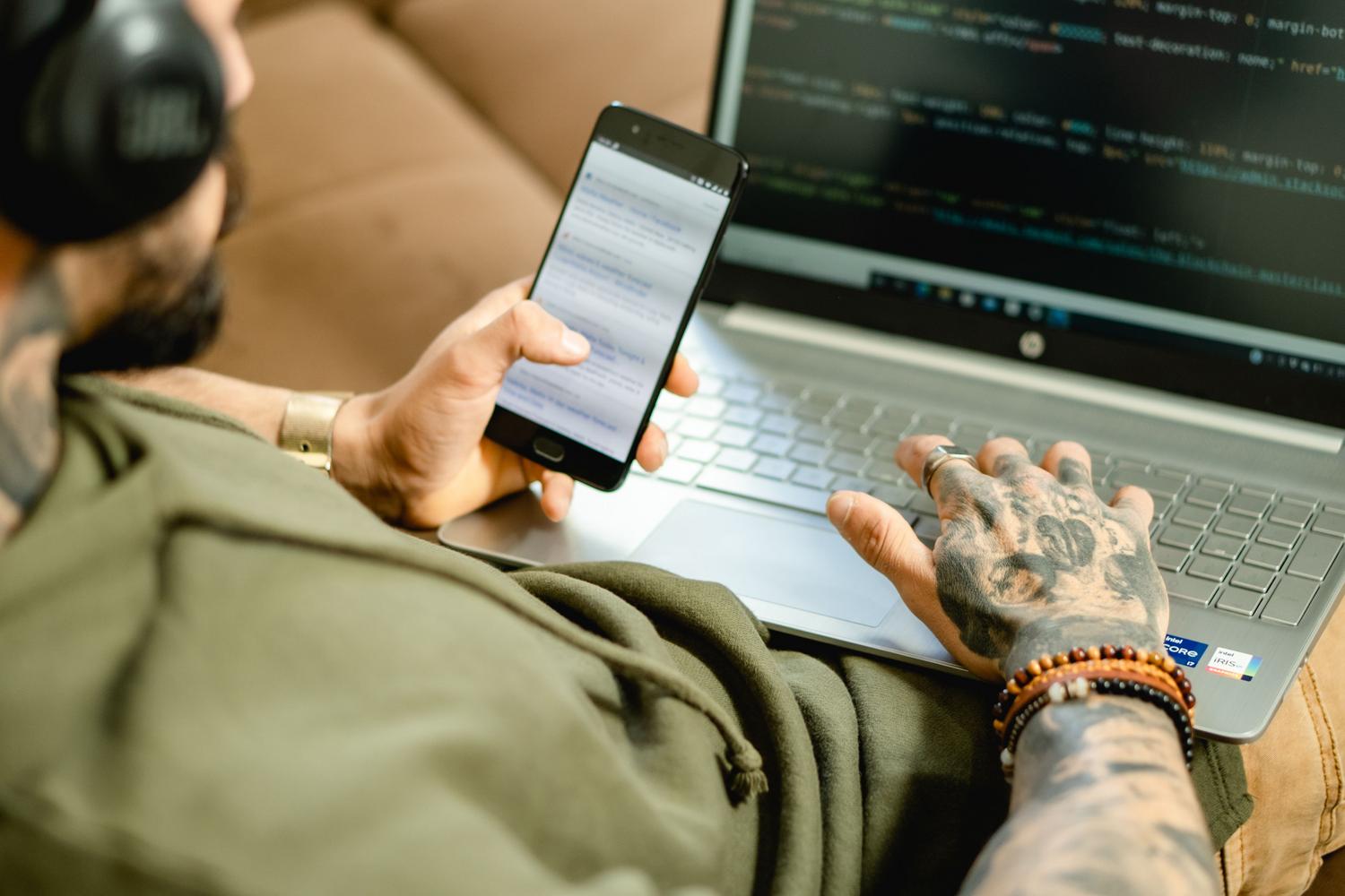 Persona utilizando un smartphone para verificar su identidad mientras trabaja en un ordenador, ejemplificando la autenticación multifactor y el modelo Zero Trust (ZTNA).