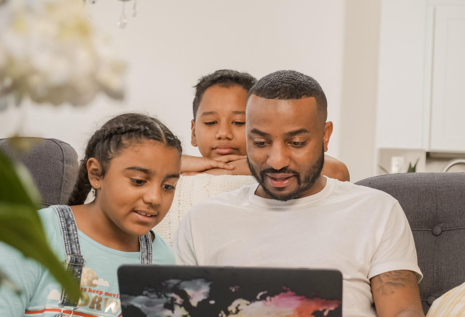 Padre e hijos compartiendo el uso de un ordenador portátil en casa, ilustrando la necesidad de perfiles independientes en equipos compartidos.