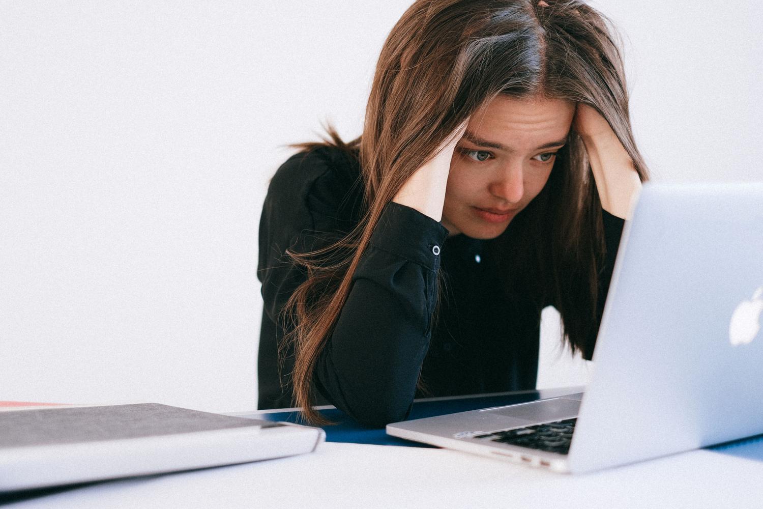 Mujer joven estresada con la cabeza entre las manos mirando la pantalla de su laptop, ilustrando la impaciencia ante un inicio lento de Windows.