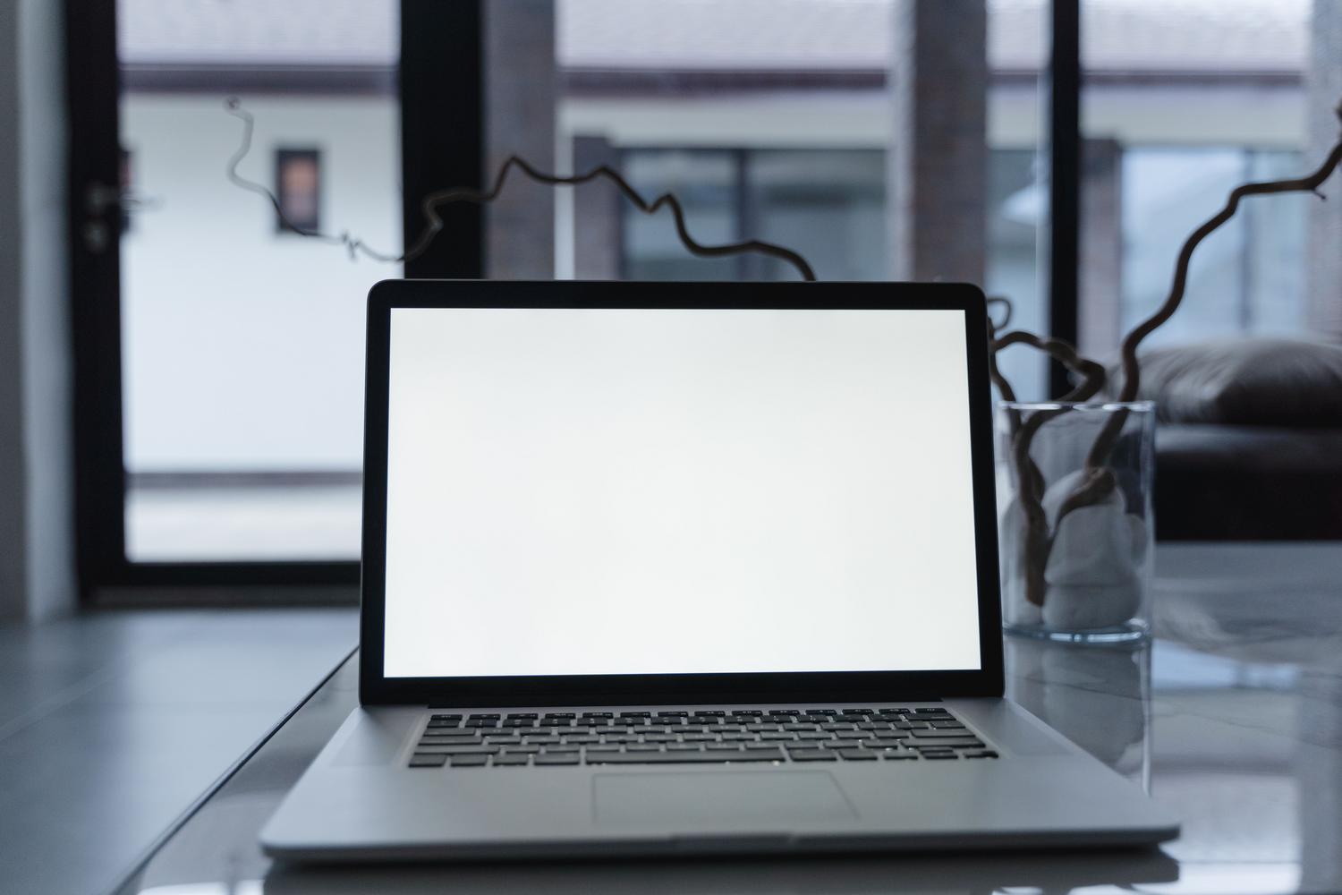 Primer plano de un ordenador portátil plateado con pantalla blanca sobre una mesa reflectante, ideal para guías técnicas de software.