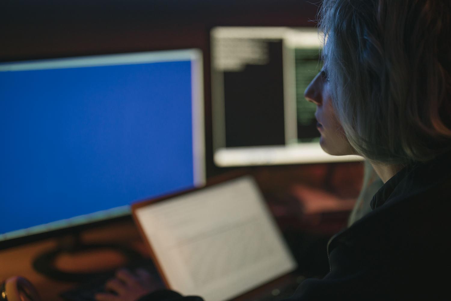 Persona trabajando en un entorno técnico con múltiples monitores, uno de los cuales muestra una pantalla azul, simulando la resolución de errores de sistema.