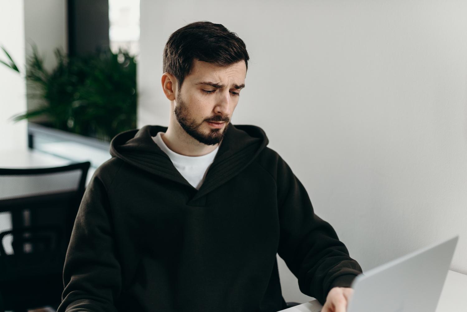 Hombre con expresión frustrada y preocupada frente a un MacBook en una oficina en casa, representando la pérdida de archivos importantes.