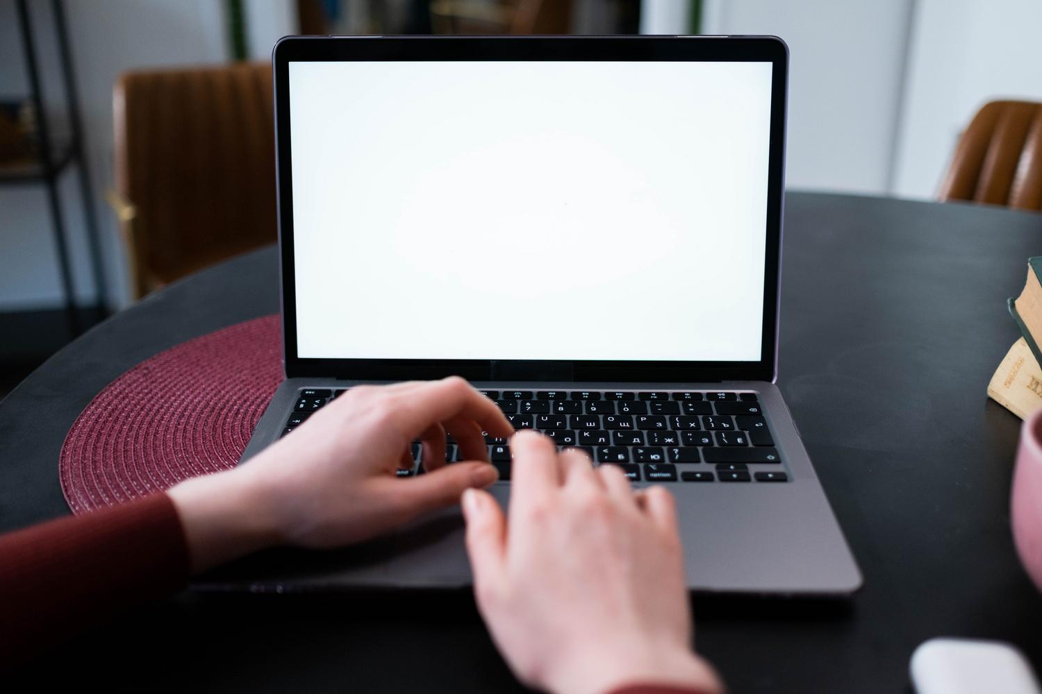 Primer plano de manos escribiendo en un teclado de portátil con pantalla blanca