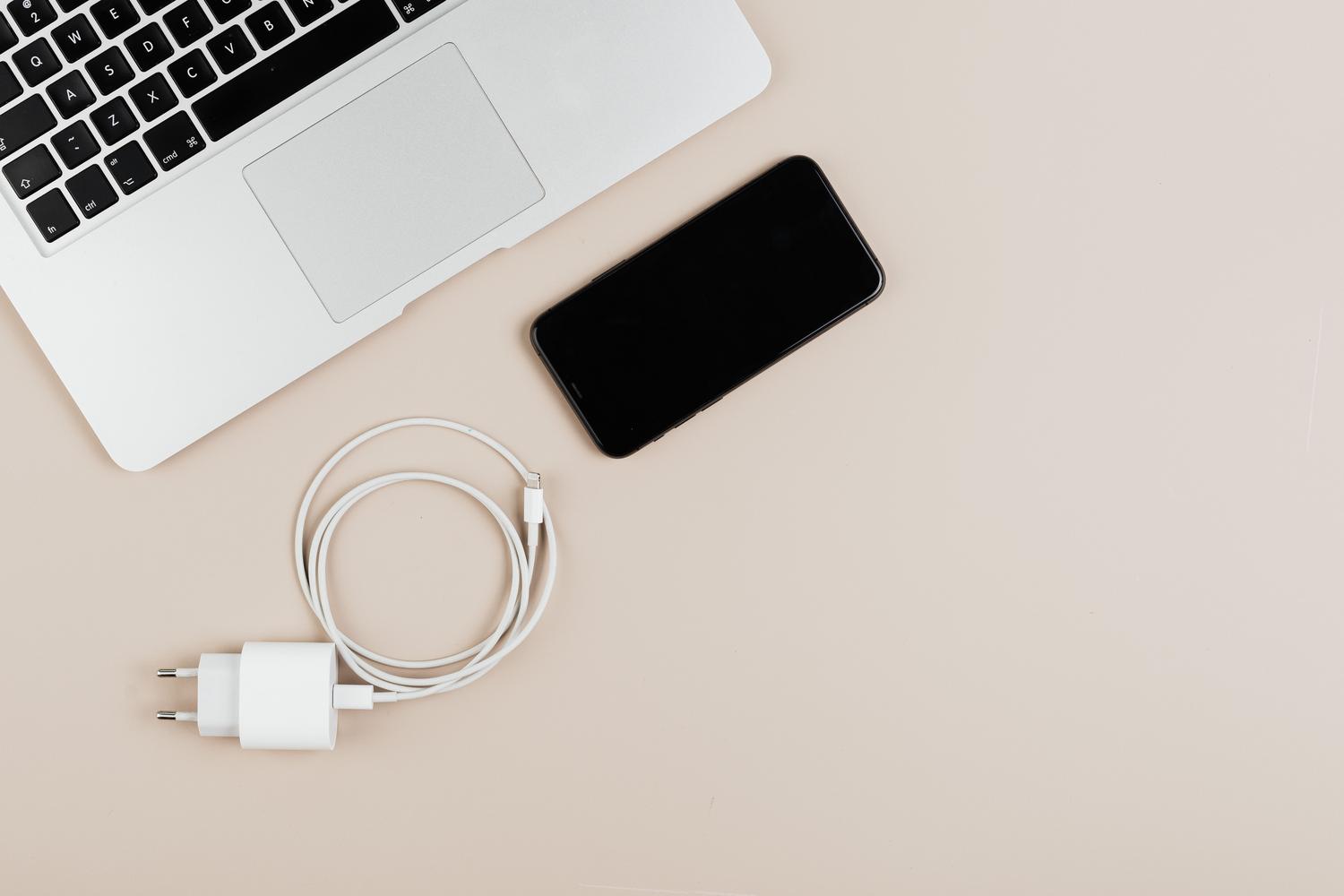 Composición minimalista de un MacBook, smartphone y cargador sobre un fondo neutro.