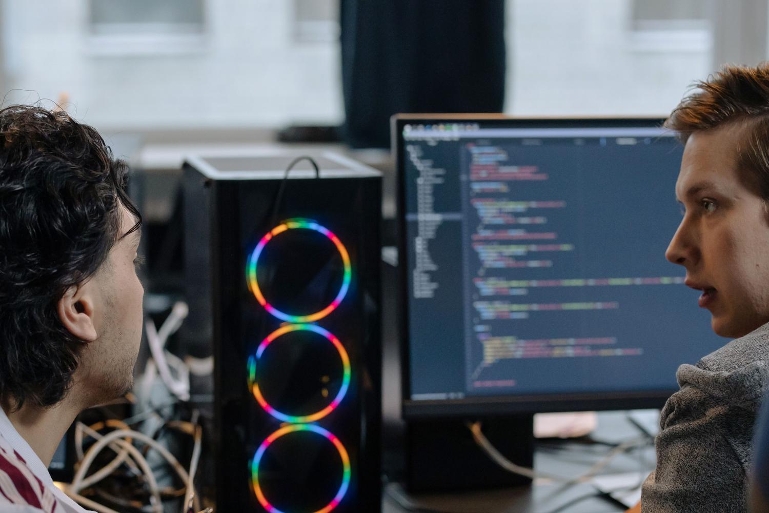 Dos programadores colaborando y revisando código en un monitor, ideal para representar Pull Requests y GitHub.