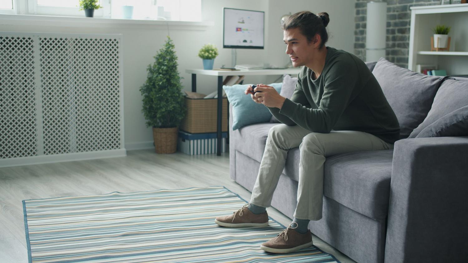 Joven relajado en el sofá de su casa disfrutando de una sesión de videojuegos.
