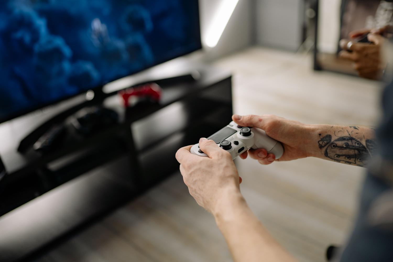 Primer plano de una persona utilizando un mando de videojuegos en un salón moderno con televisión.