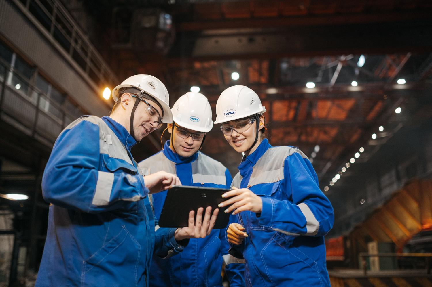 Equipo de ingenieros colaborando y analizando datos en una tablet dentro de una fábrica, representando la integración IT/OT.