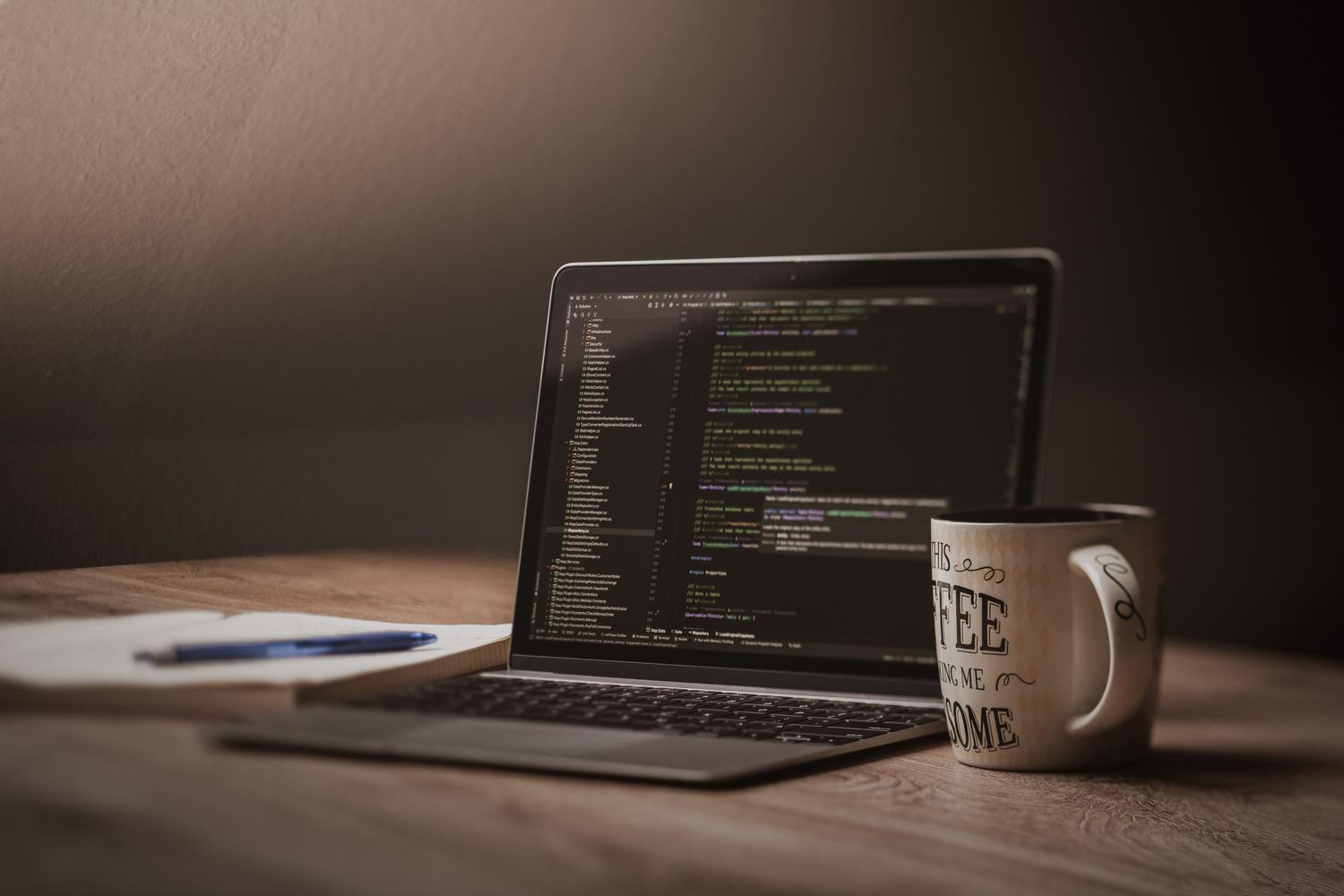 Espacio de trabajo acogedor de un programador con portátil, café y bloc de notas para planificación de código.