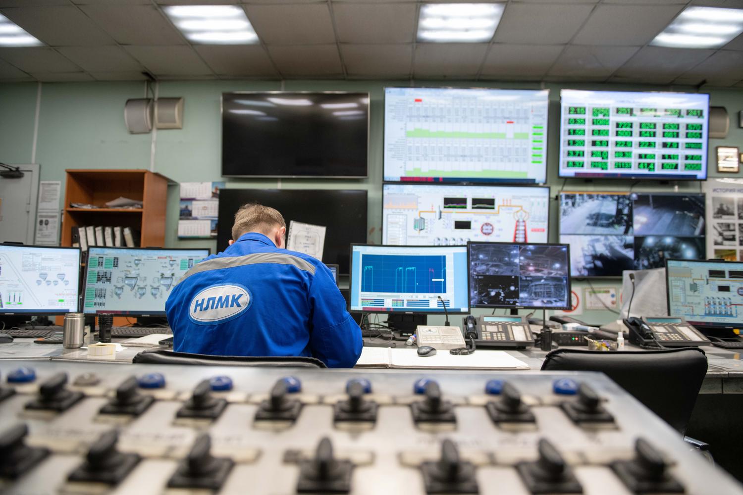 Ingeniero supervisando múltiples pantallas de control en una sala de mando industrial para la monitorización de datos en tiempo real.