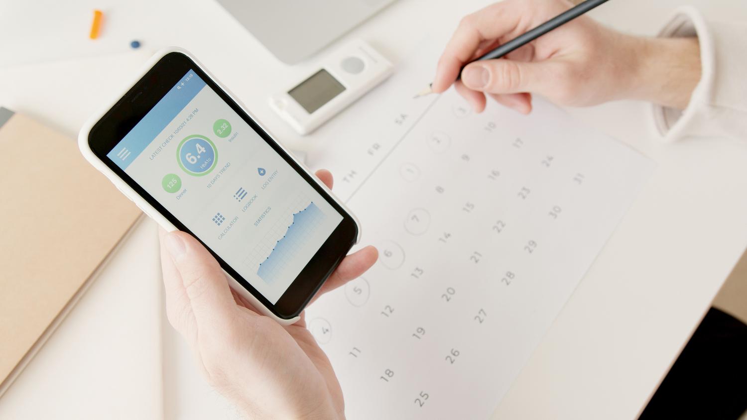 Uso de una aplicación de salud en un smartphone junto a un calendario y diario de registro médico.