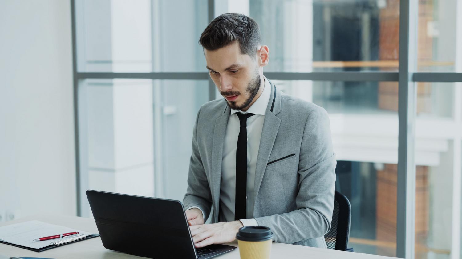 Administrador de IT en una oficina corporativa moderna gestionando la flota de dispositivos de la empresa a través de su portátil.
