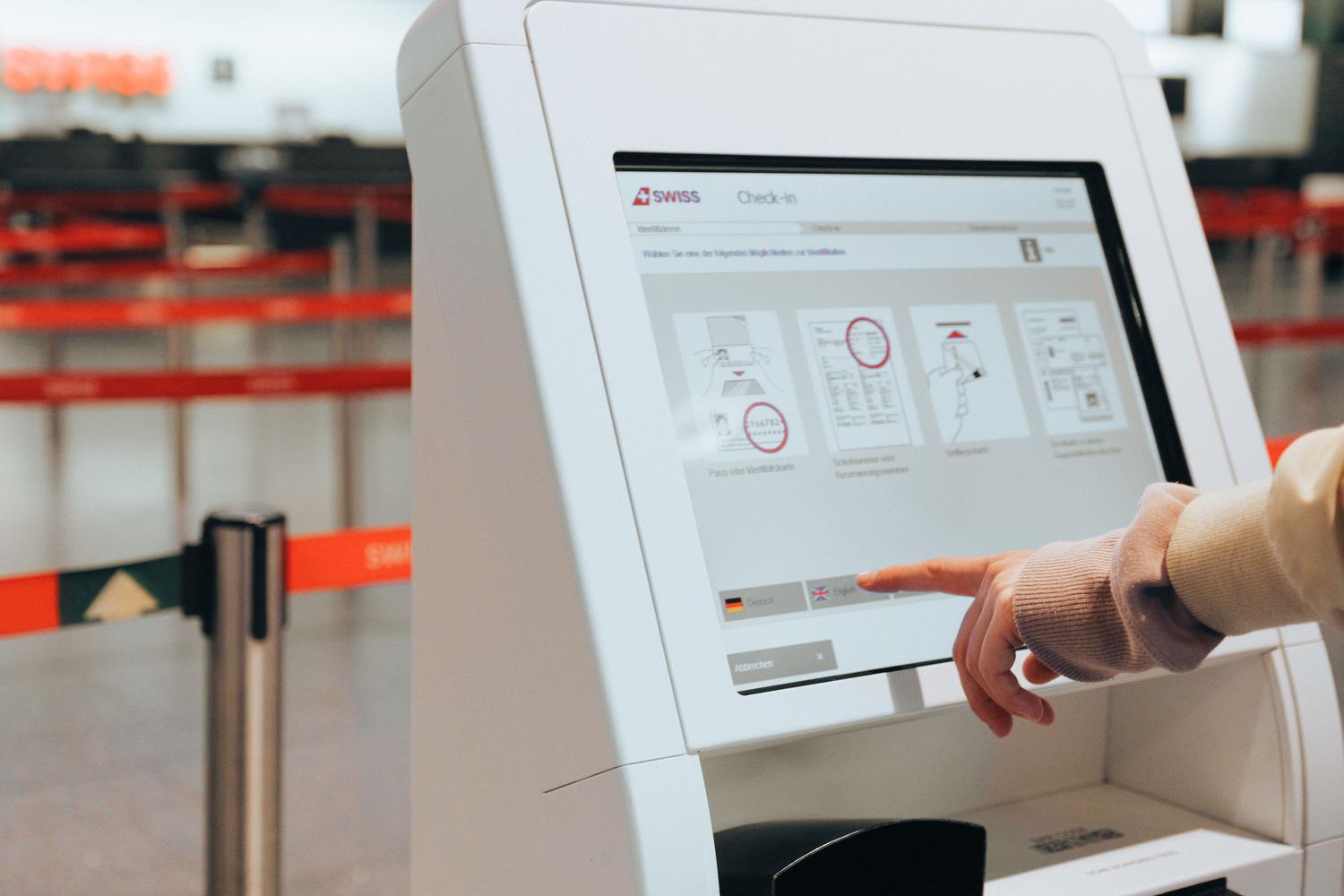 Persona utilizando un kiosco de auto-check-in en un aeropuerto, ilustrando la interacción táctil en entornos profesionales.