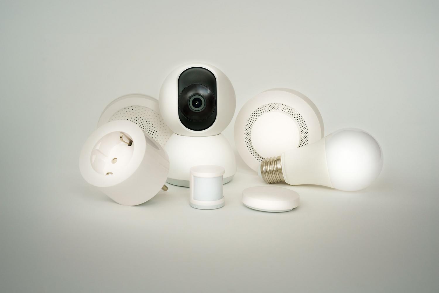 Conjunto de dispositivos de automação residencial, como lâmpadas e tomadas inteligentes, sobre um fundo branco.