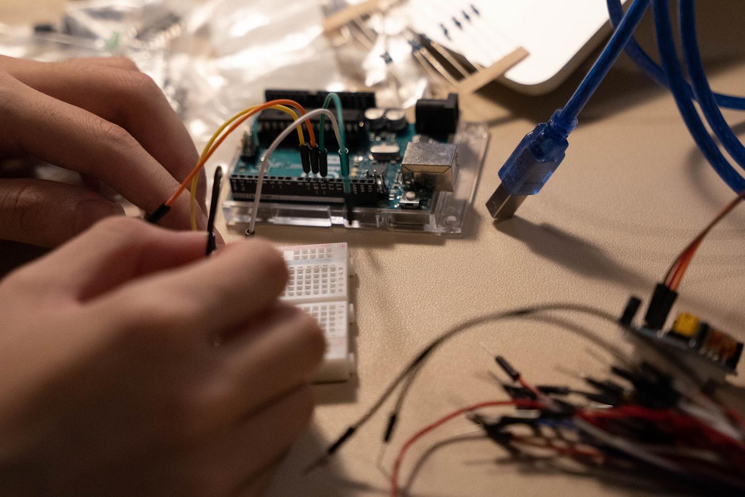Primer plano de manos conectando cables jumper en una placa de pruebas con un microcontrolador.