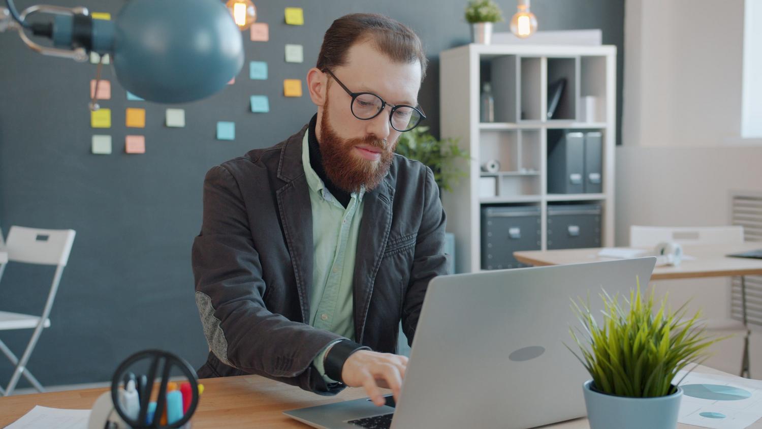 Hombre trabajando con un portátil en una oficina moderna, simbolizando el uso de herramientas de productividad basadas en la nube.